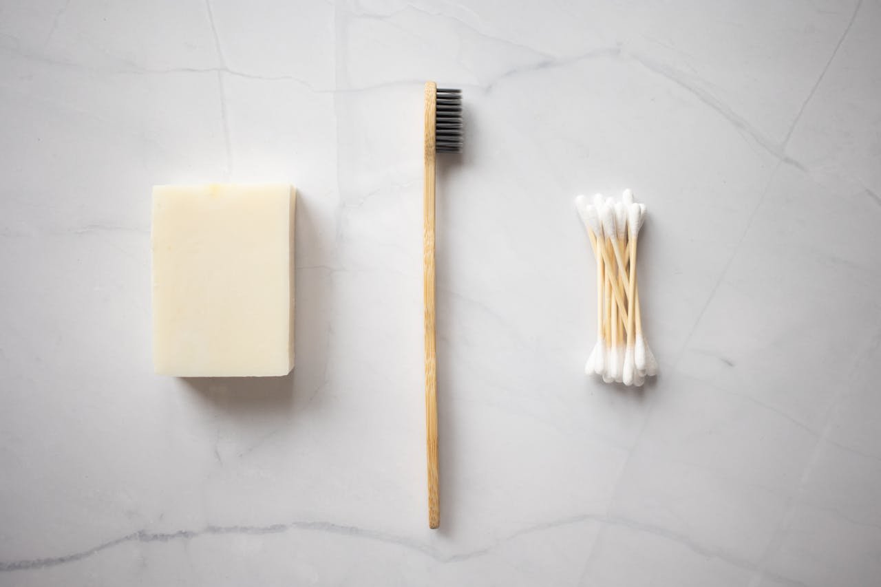 From above of bamboo toothbrush placed between organic soap and wooden ear sticks placed on marble table